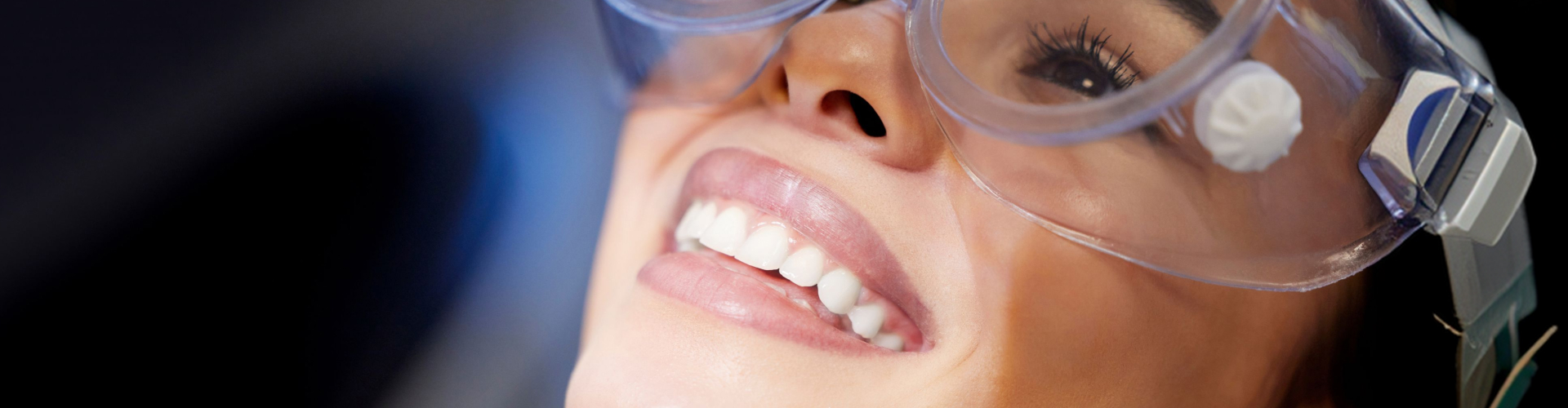 Close-up of a smiling patient wearing protective eyewear during a professional teeth whitening treatment.